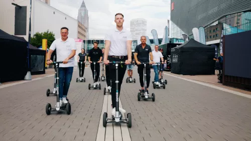 Viele jungen Menschen fahren in Formation mit dem XBoard auf ein Messegelände.