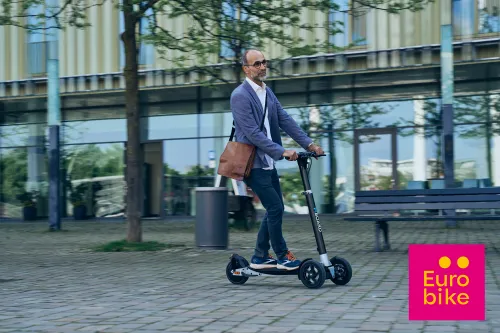 Mann fährt XBoard E-Scooter auf modernem Campus – Eurobike 2025 Logo unten rechts im Bild